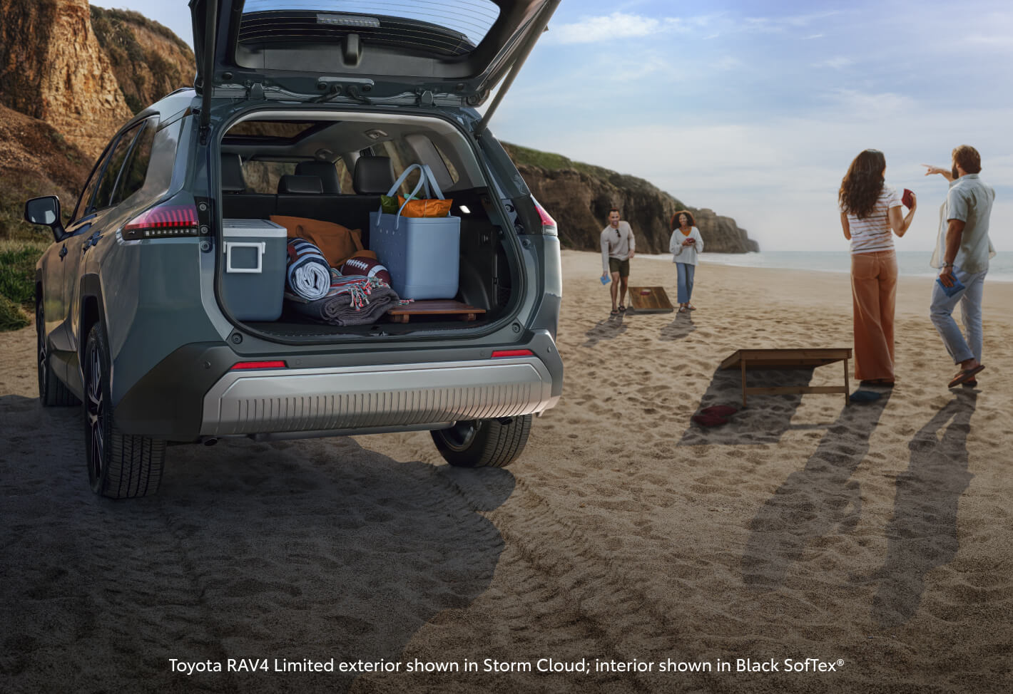 Rear view showing an open trunk of a Toyota RAV4 Limited on a beach while a family plays by the ocean.
