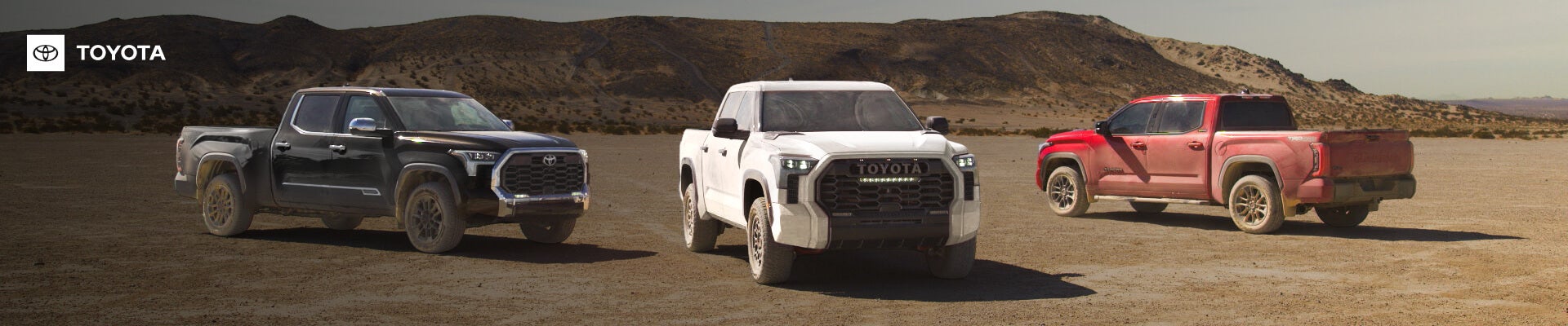 AFront view of three 2026 Toyota Tundra trucks parked side-by-side on an expansive, dusty desert.