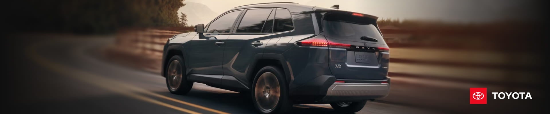 Dark Toyota RAV4 driving on a road, shown from a rear three-quarter view with Toyota branding on the right.