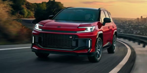 Red Toyota RAV4 Hybrid driving on a curved road at sunset, shown from a front three-quarter view.